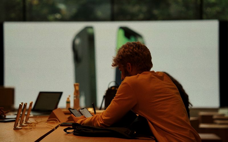 Cliente de costas numa loja de eletrônicos, comparando dois celulares, um em cada mão